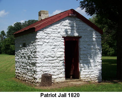 Color photo: Whitewashed 8 by 8 stone building with single door, chimney, tiny window